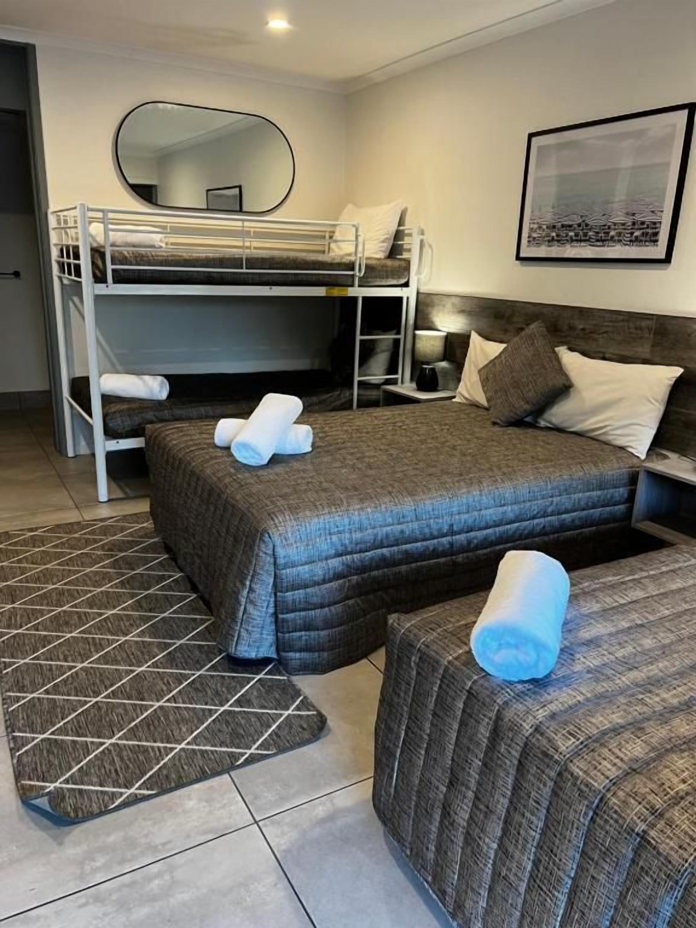A room with a bunk bed, a single bed, a bedside table with a lamp, and a framed picture on the wall.