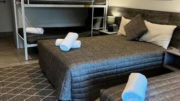 A room with a bunk bed, a single bed, a bedside table with a lamp, and a framed picture on the wall.