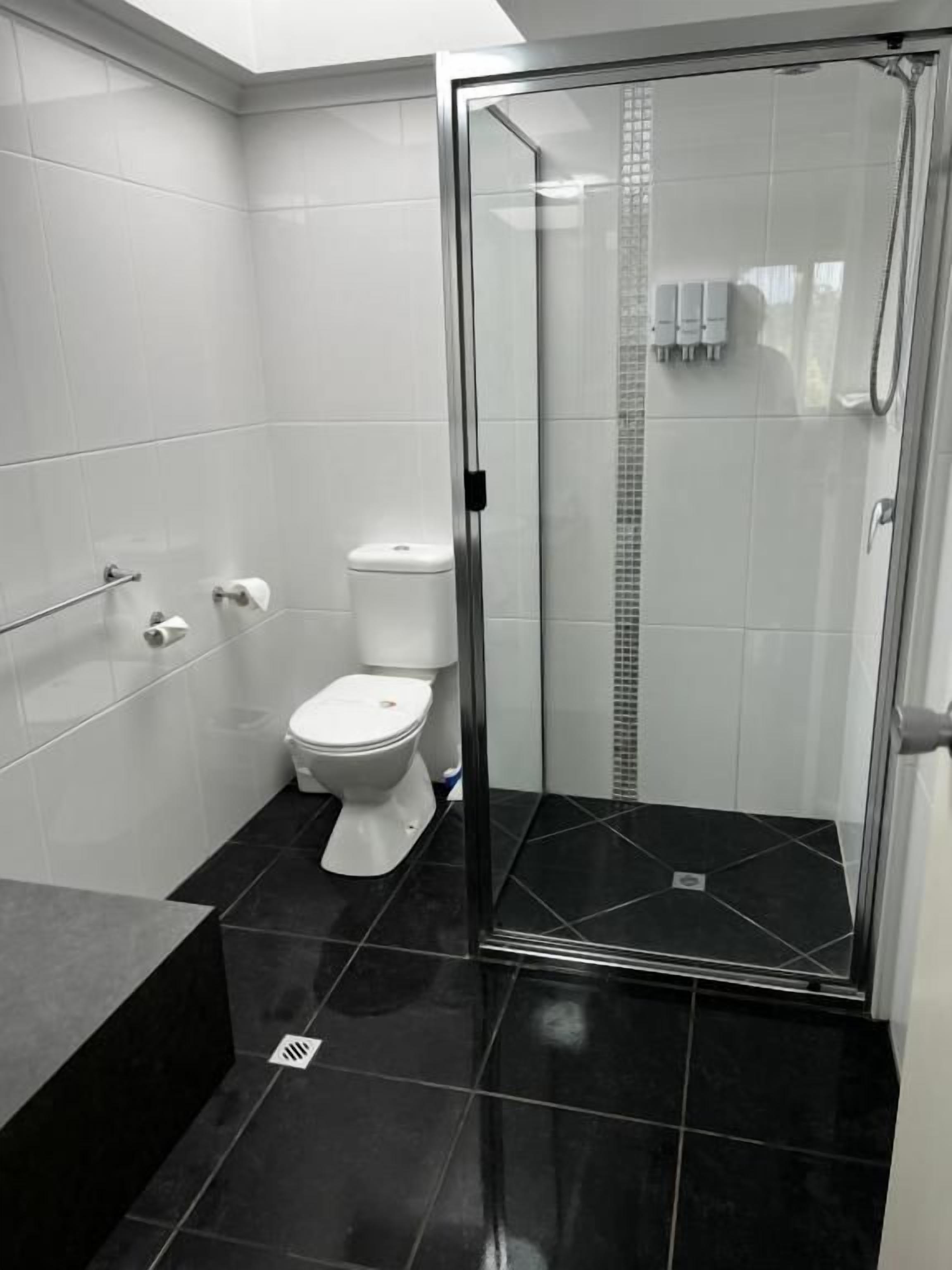 Et moderne badeværelse med et glasafskærmet brusebad, toilet og sort flisegulv.