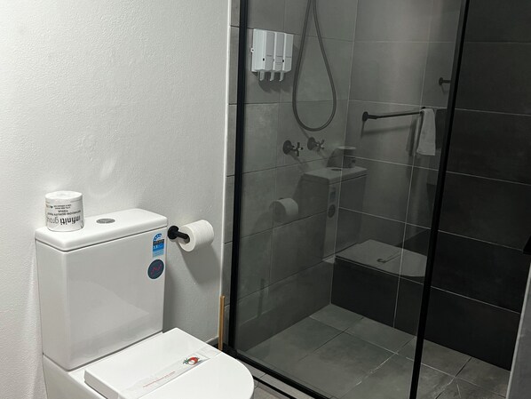 A bathroom with a toilet, a glass shower enclosure, and a white sink.