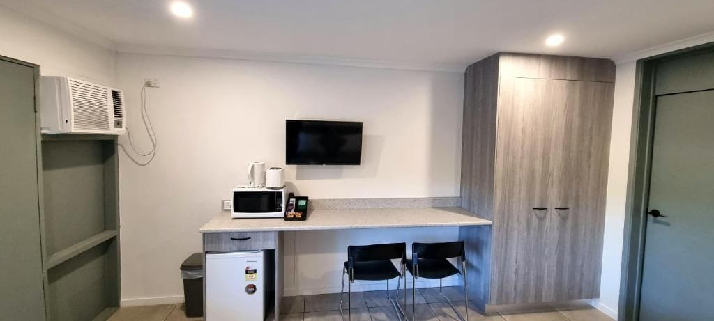 A compact kitchenette with a microwave, a small refrigerator, a sink, and a flat-screen TV mounted on the wall.