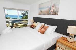 A bedroom with a large bed, a nightstand, a lamp, and a painting of a beach scene.