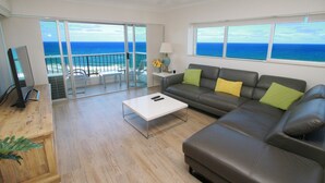 A living room with a sofa, a coffee table, and a TV. There is a balcony with a view of the ocean. - Narrowneck Court (Surfers Paradise)