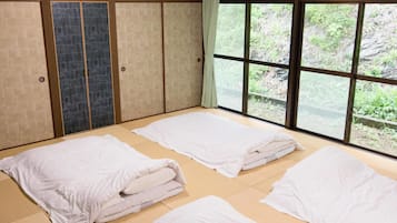 A room with tatami flooring, a large window with a view of greenery, and a sliding door with a textured pattern.