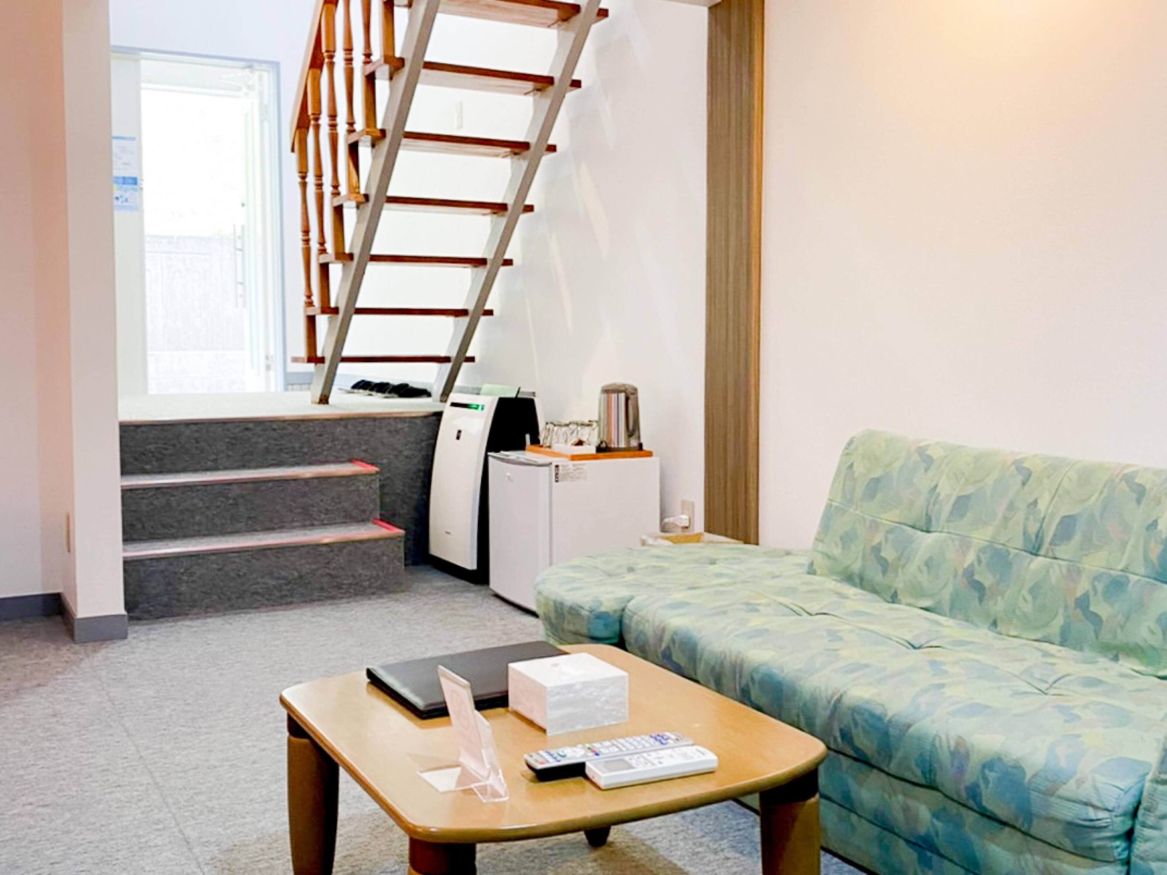 Habitación de hotel con escalera, sofá, mesa de centro con una computadora portátil, control remoto y un mueble pequeño.