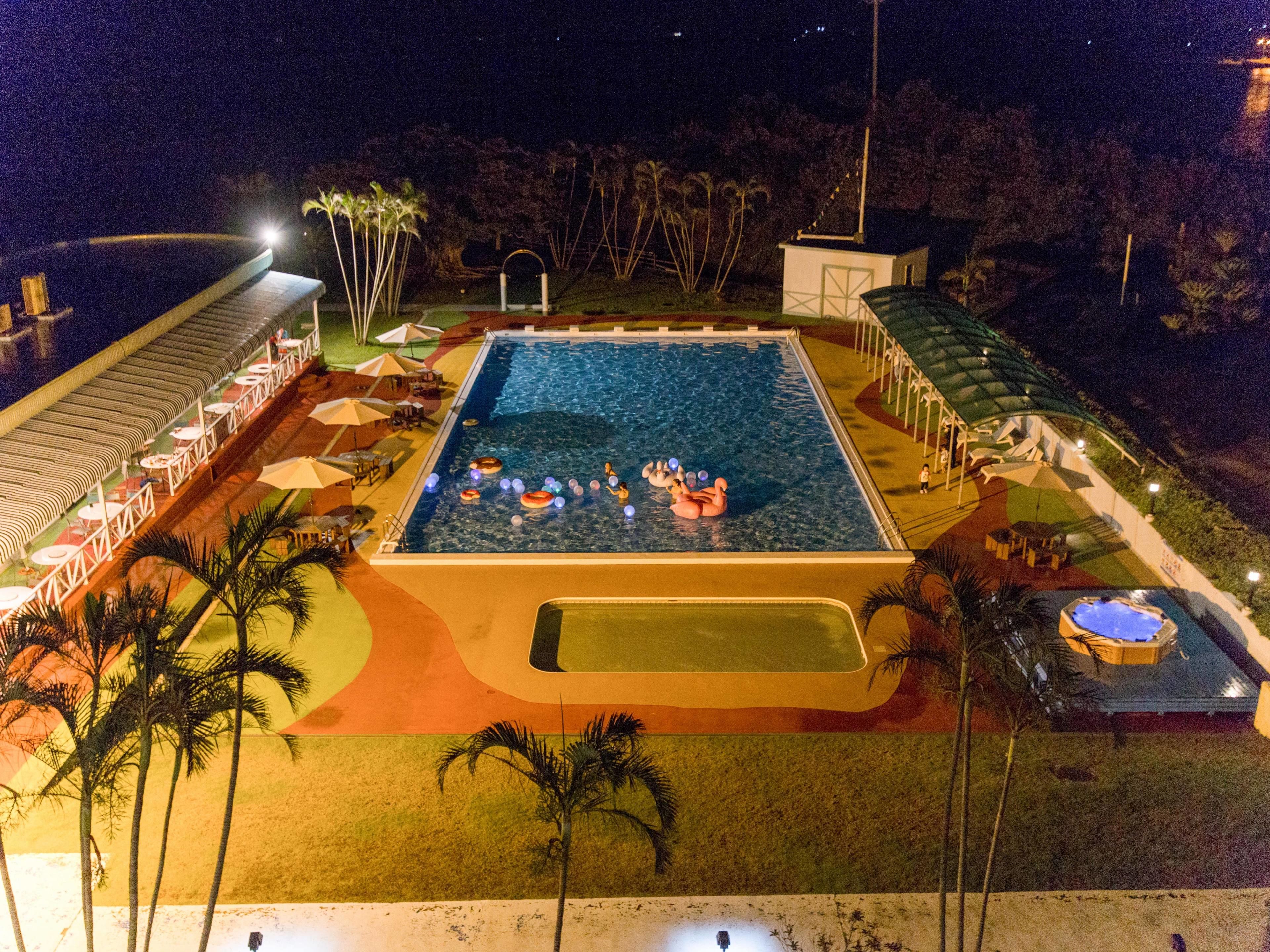 Ein großer Pool mit Liegeinsel, umgeben von Liegestühlen und Sonnenschirmen, sowie ein kleinerer Whirlpoolbereich.
