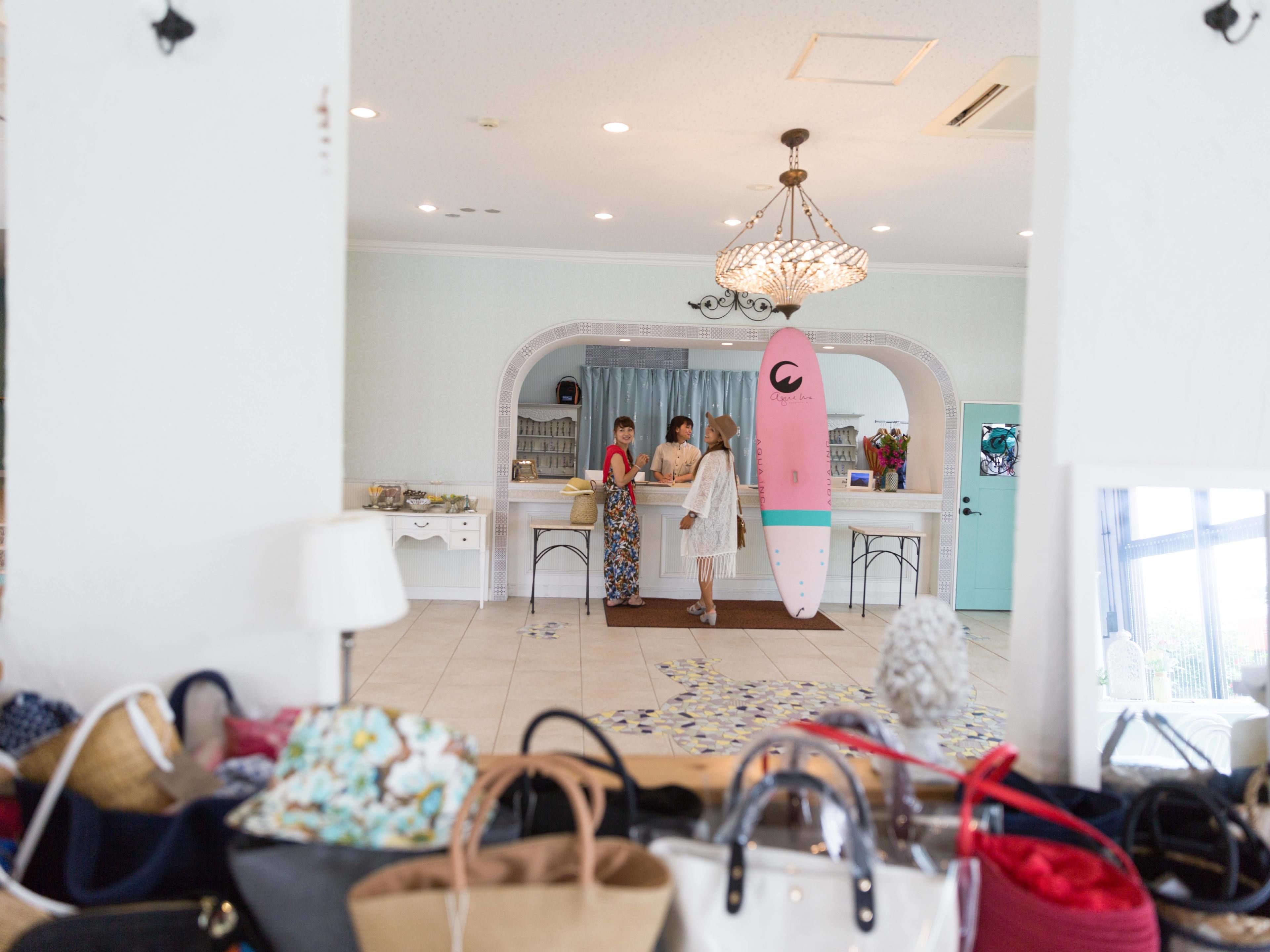 A hotel lobby with a reception desk, a surfboard decoration, and multiple handbags on the floor.