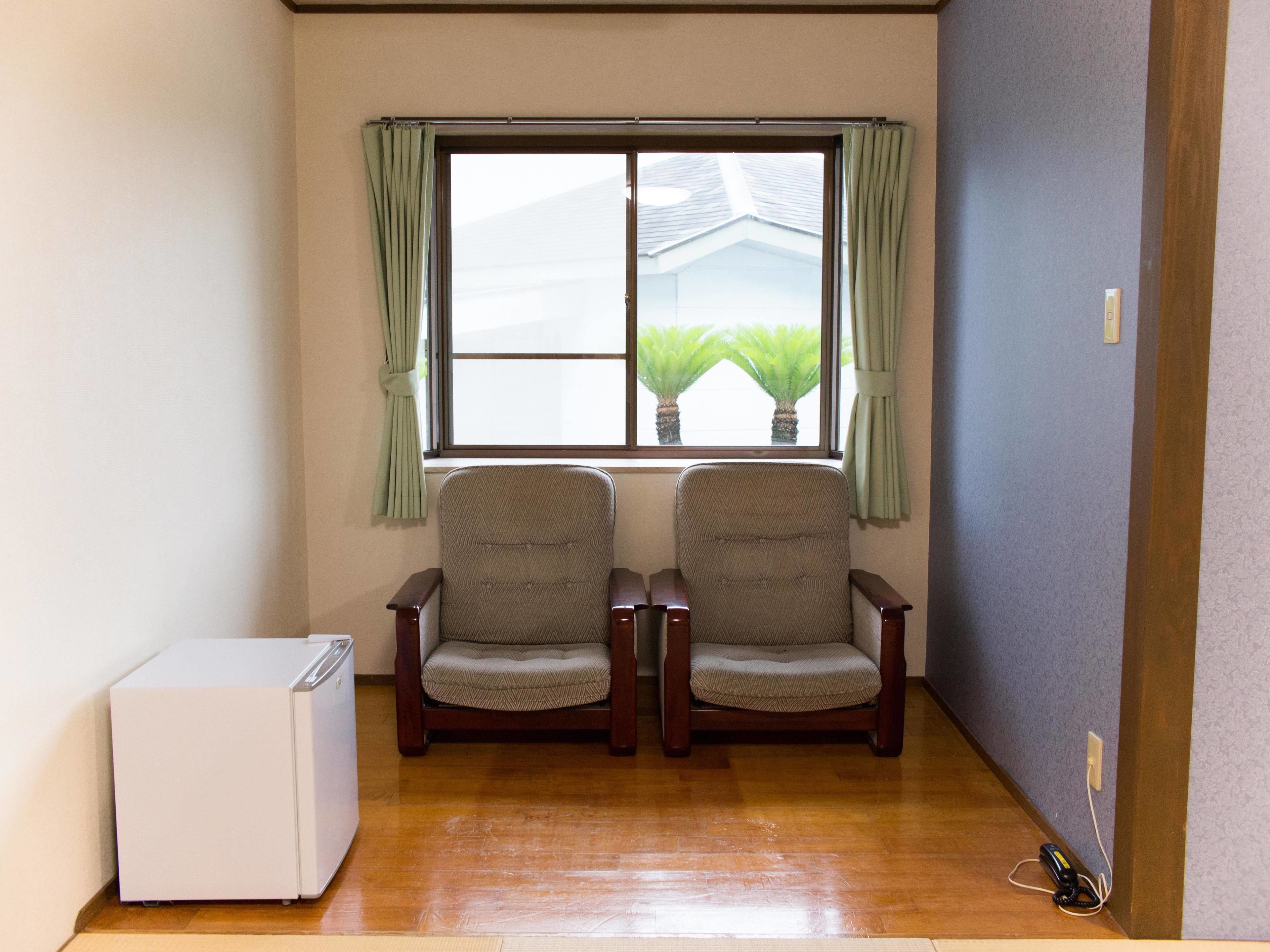 A room with two wooden chairs, a white refrigerator, and a window with curtains.