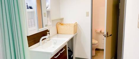 Un baño con un lavamanos blanco, un mueble de madera y una cesta de mimbre sobre la encimera.