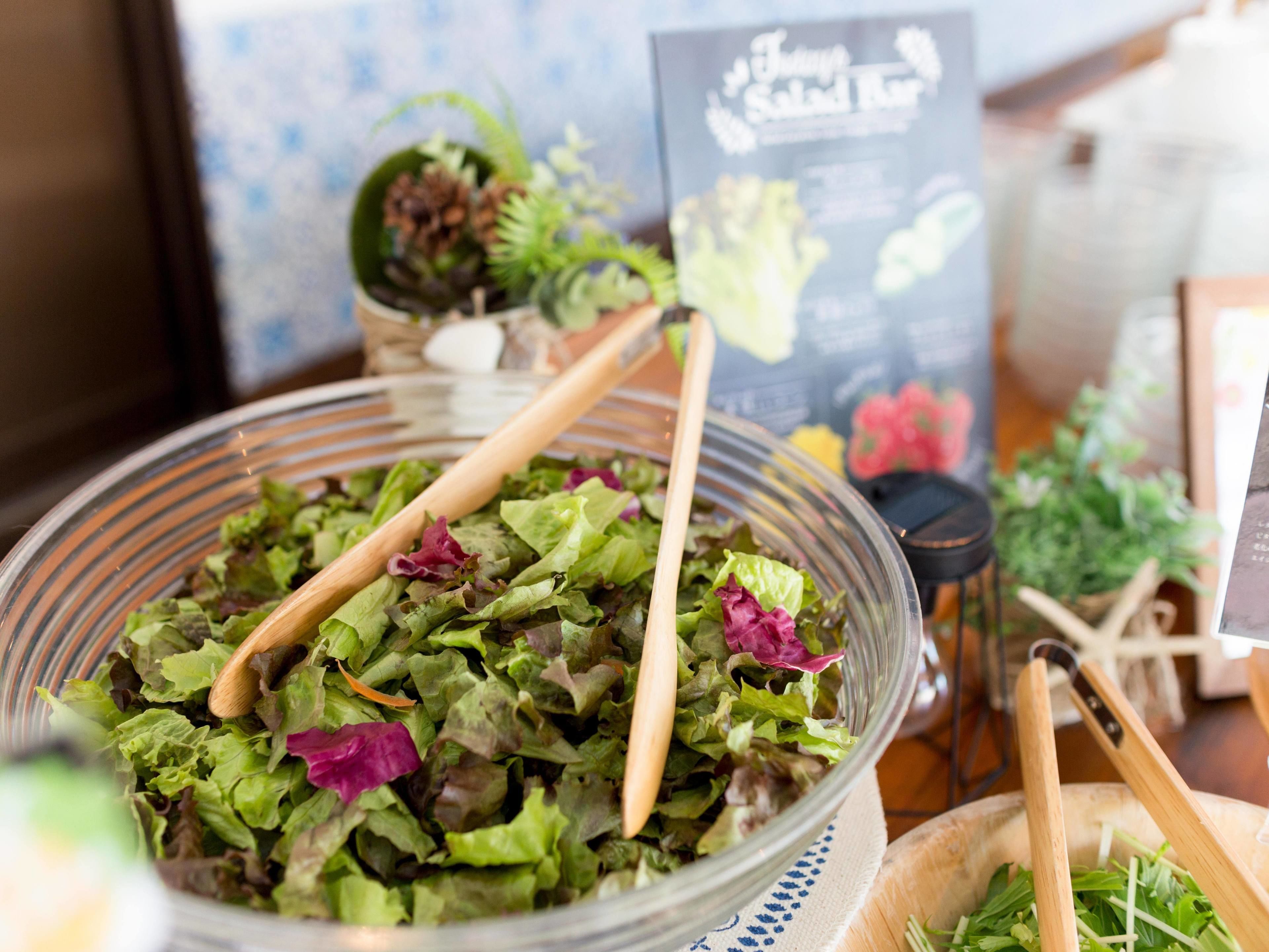 Un saladier rempli de différentes sortes de légumes verts, une cuillère en bois, un panneau affichant le menu en arrière-plan et une petite plante en pot.