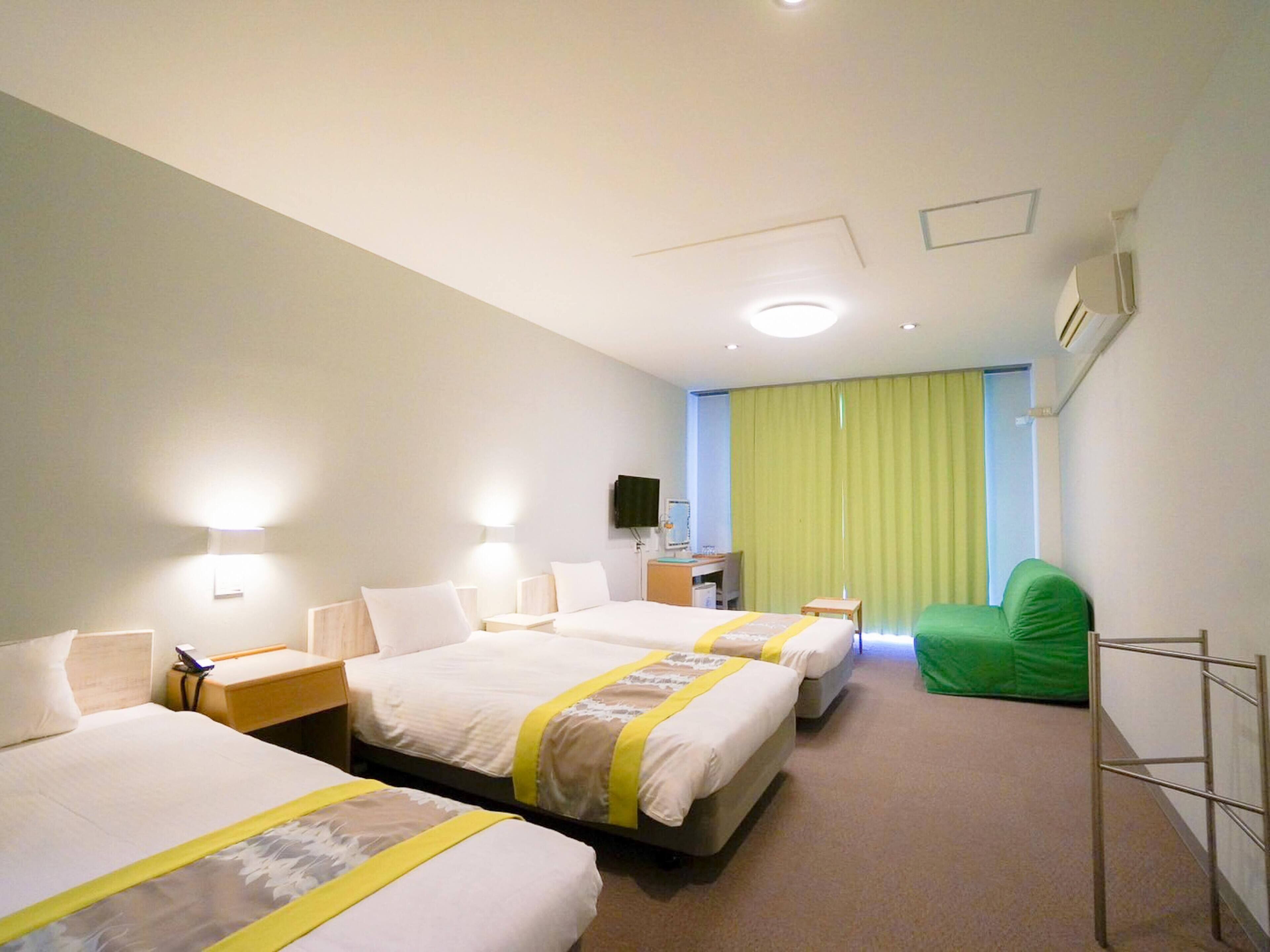 Una habitación de hotel con tres camas, un escritorio, una silla y un televisor.
