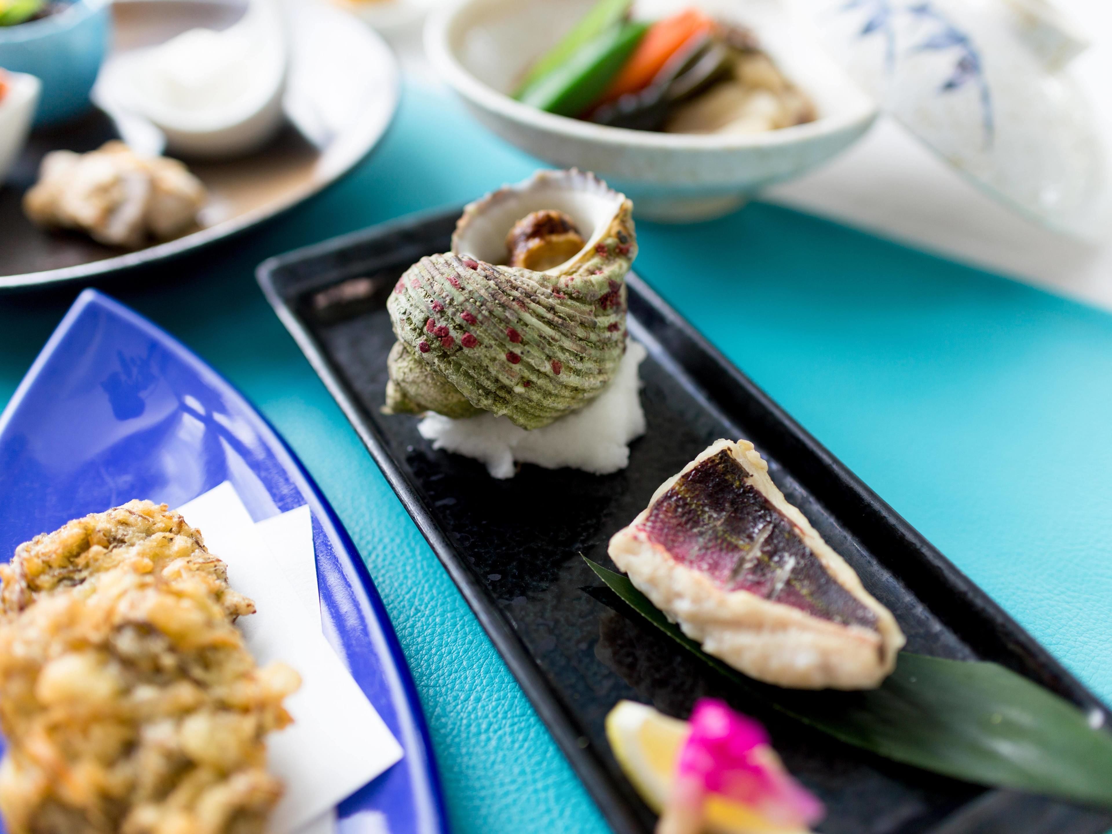 A tray with sushi, a piece of meat, and a decorative item on a blue table.