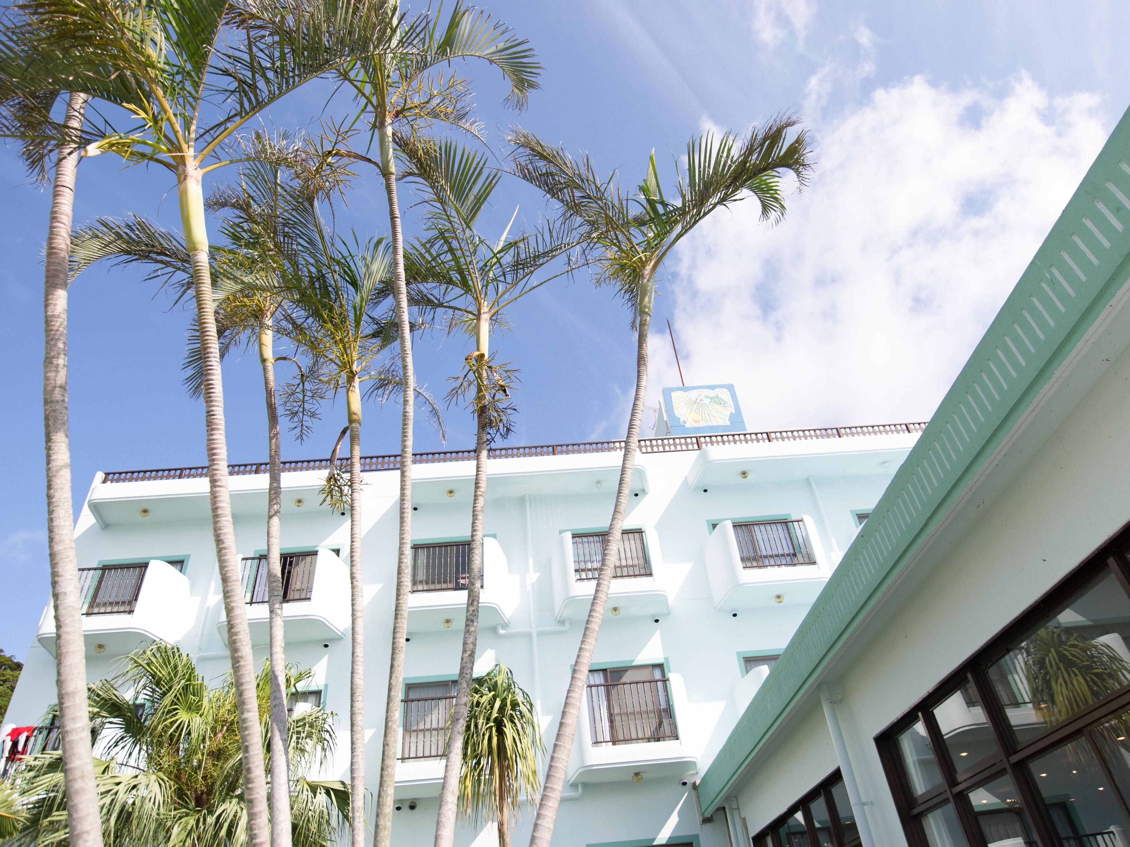 A multi-story building with balconies and palm trees.