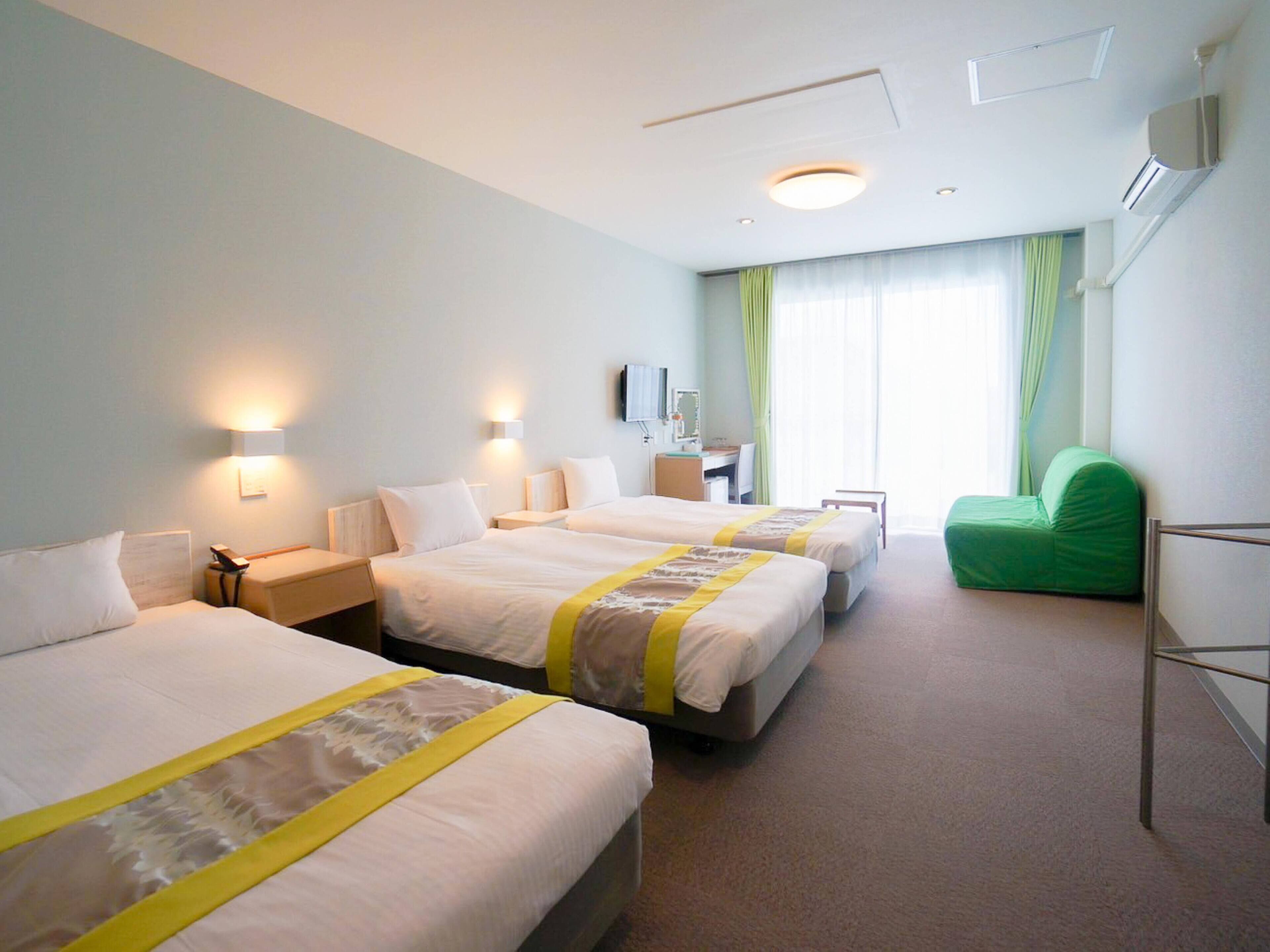 A hotel room with three beds, a desk, a chair, and a TV.