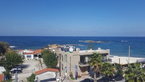 Un edificio costero con terraza en la azotea, una playa al fondo y un cielo azul despejado.