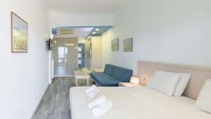 Habitación de hotel moderna con una cama grande, un sofá azul, una pequeña mesa con una planta y vistas al pasillo.