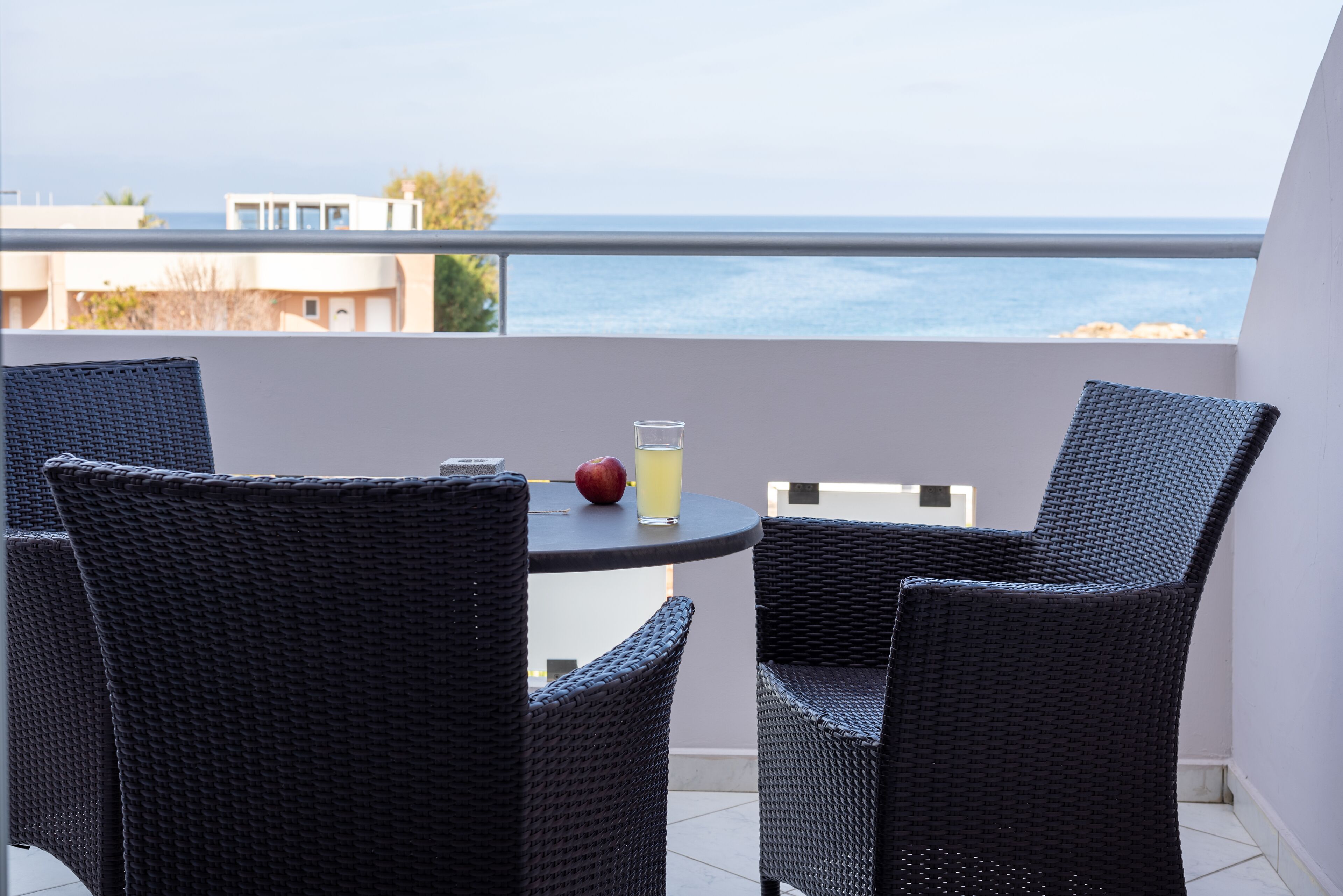 A balcony with wicker chairs, a small round table, and a glass of drink.