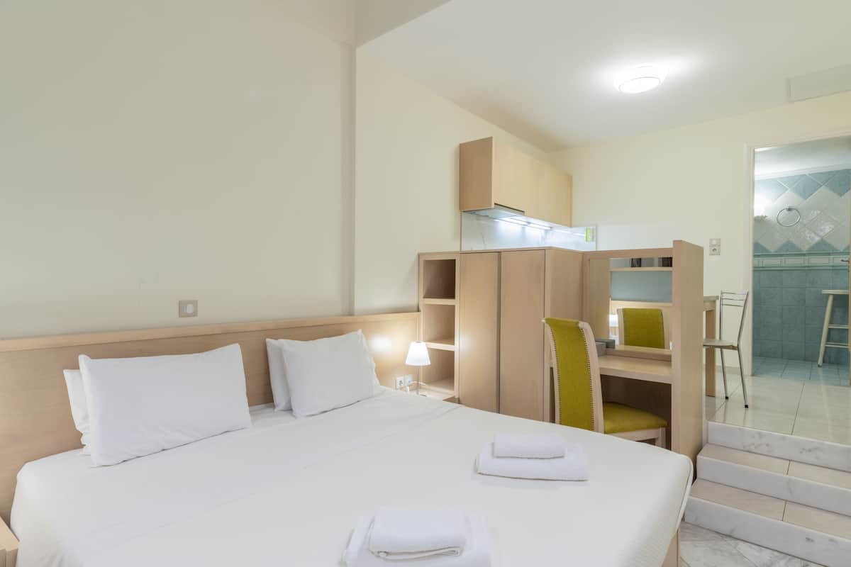Une chambre d’hôtel avec un grand lit, un bureau et une chaise. On peut voir la salle de bain, qui comprend une douche et des toilettes, à travers une porte ouverte.