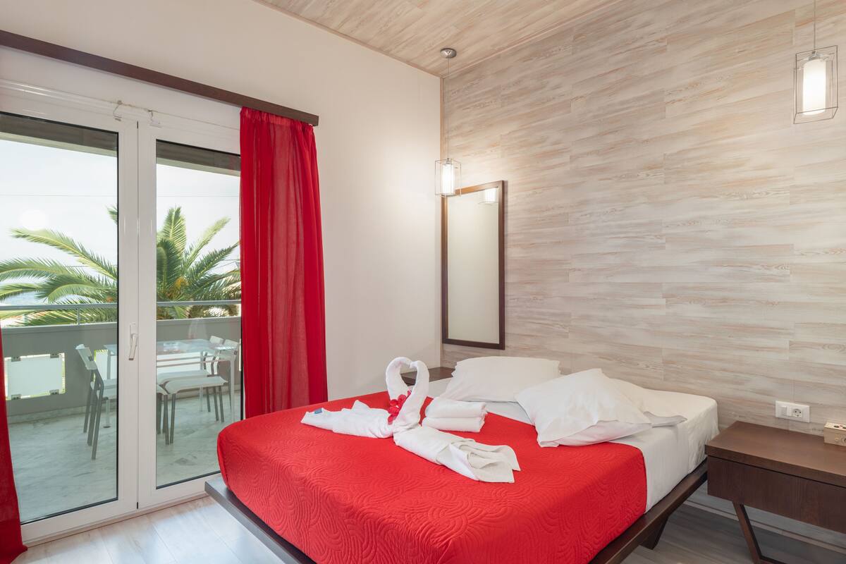 Une chambre d’hôtel avec une couvre-lit rouge, un balcon avec des rideaux rouges et un mur en bois.