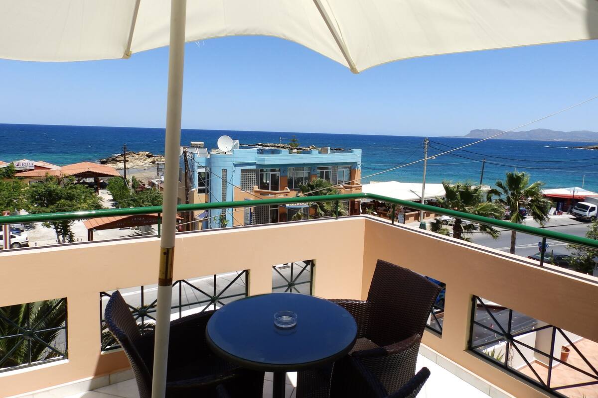 Un balcon avec une table et des chaises, donnant sur une plage et l’océan.