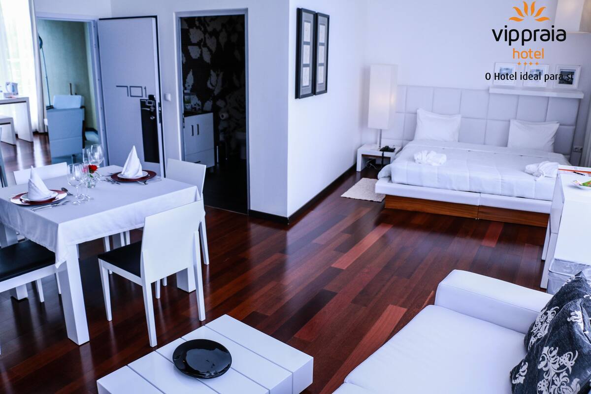 A modern hotel room with a dining area, a sofa, and a bed.