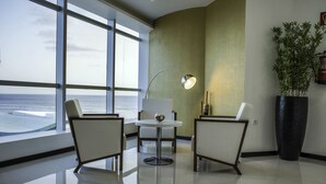 Una habitación moderna con un ventanal grande, una mesa redonda, dos sillas, una lámpara de pie y una planta de gran tamaño en maceta.