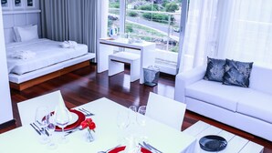 Una habitación de hotel moderna con una cama, un área de estar con un sofá y una mesa lista para comer, y vistas al exterior.