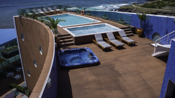 Área de piscina en la azotea con dos jacuzzis, sillones de descanso y barandilla de vidrio con vista al océano.