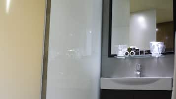 A modern bathroom with a glass shower enclosure, a white sink, dark cabinets, and a mirror above the sink.