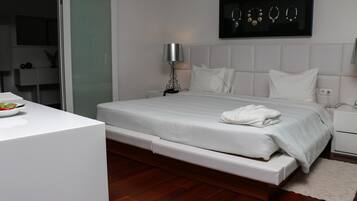 Un dormitorio moderno con cama, mesitas de noche, una mesita auxiliar, un expositor de joyas en la pared y un escritorio blanco con un cuenco de fruta.