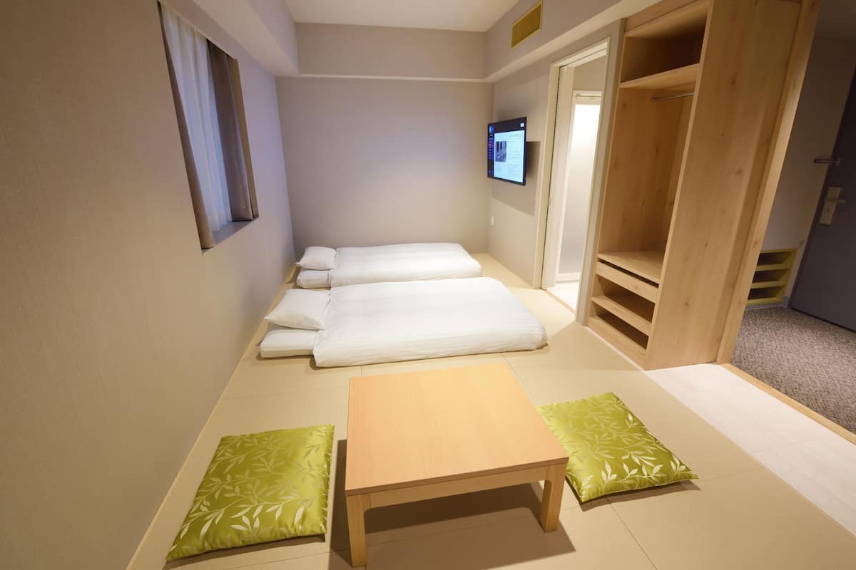 Une chambre avec deux lits, une petite table et un téléviseur fixé au mur.