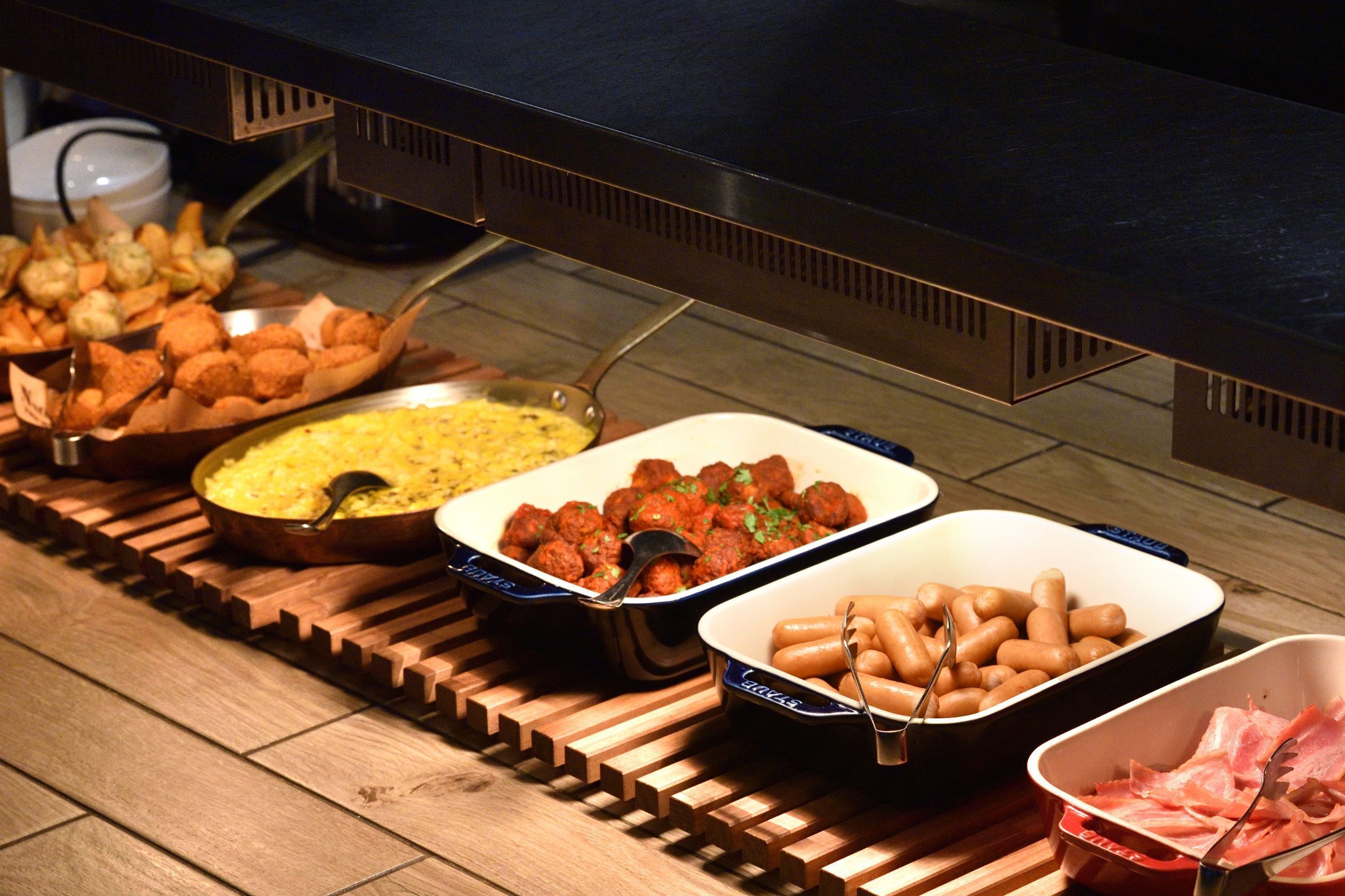 A buffet with various dishes including meatballs, sausages, and other prepared foods.