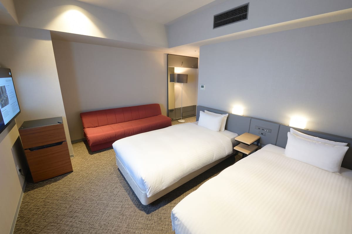 Une chambre d’hôtel avec deux lits, un canapé, un bureau et une télévision.