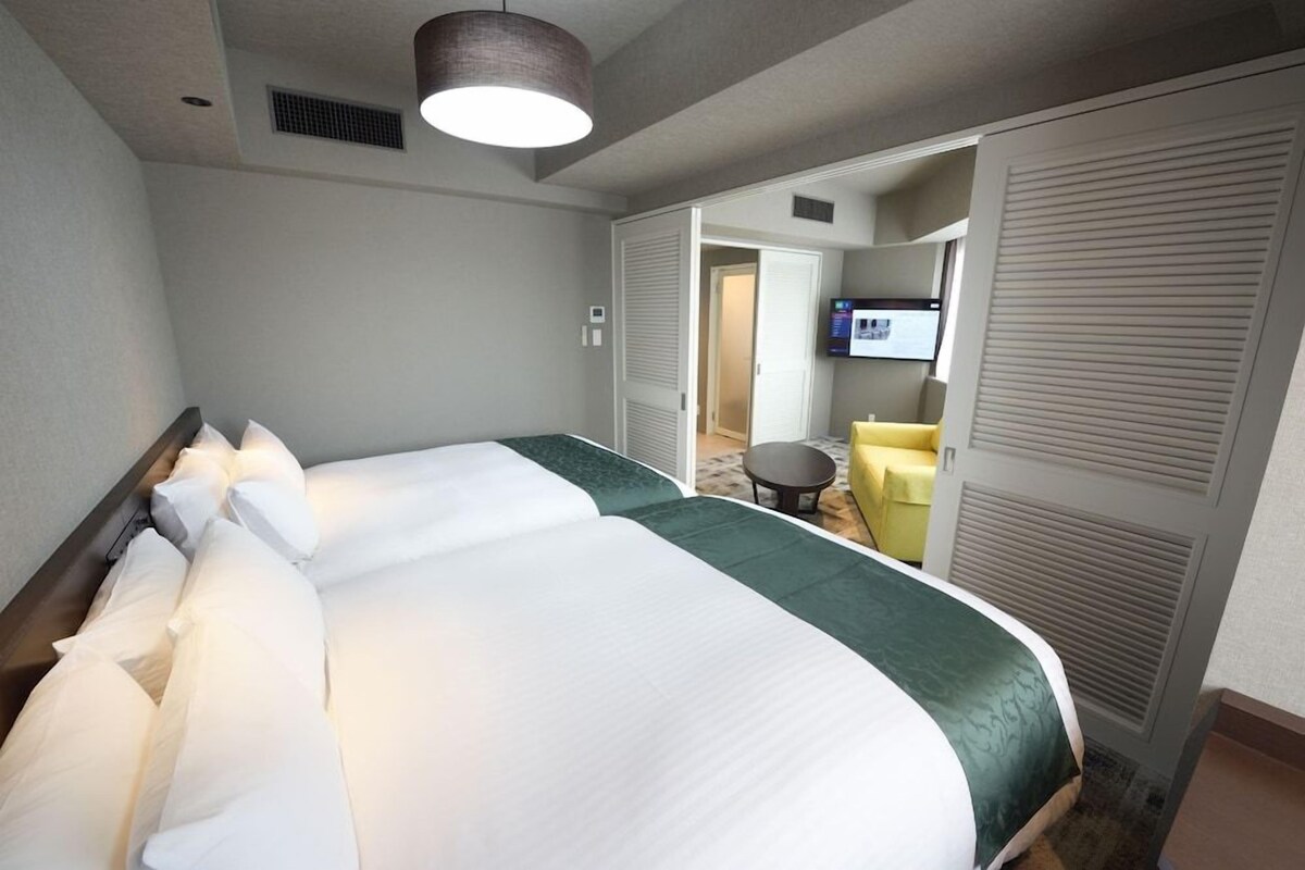 Une chambre d’hôtel avec un grand lit, une télévision et un coin salon avec un fauteuil.