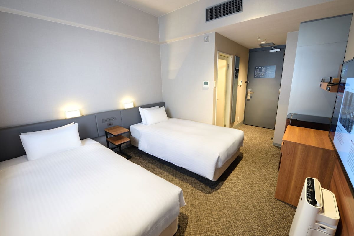 Une chambre d’hôtel avec deux lits simples, un bureau, une chaise, une télévision et un mini-bar.