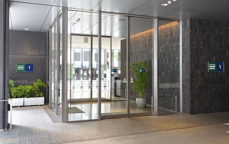 A modern hotel entrance with glass doors, a reception desk, and directional signs.