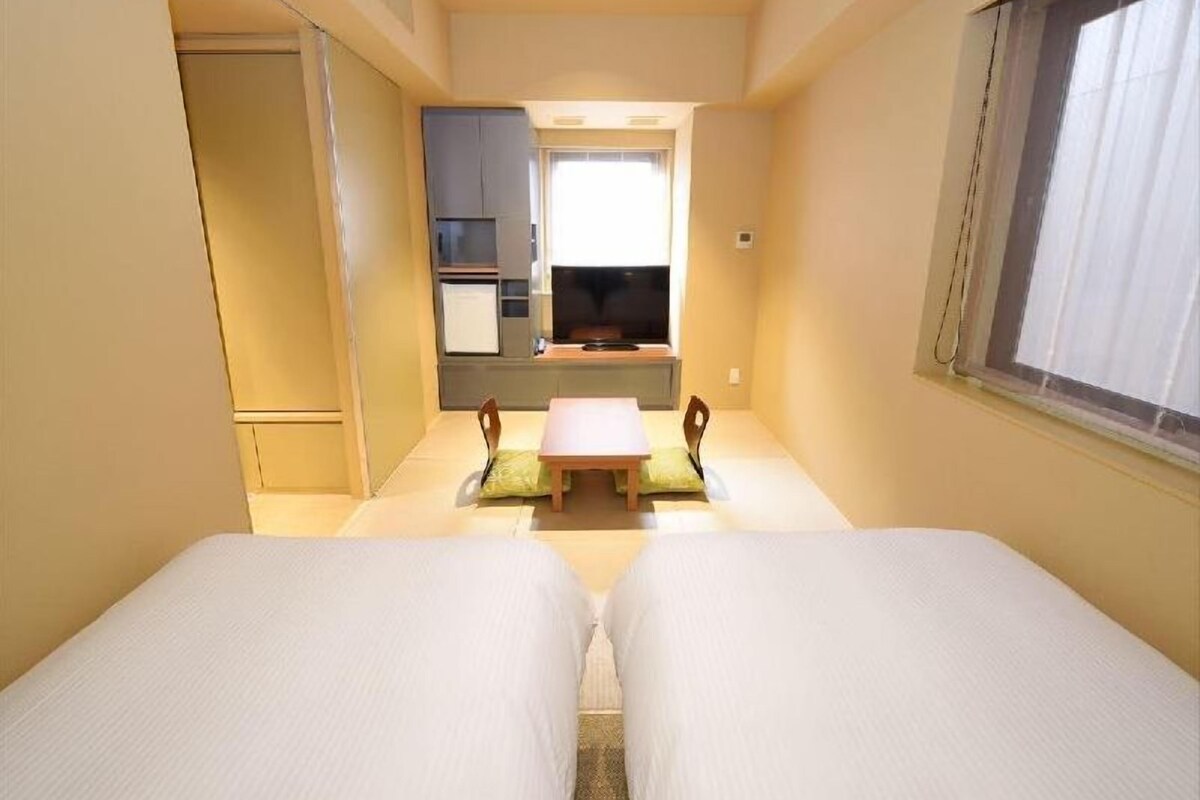 Une chambre d’hôtel avec deux lits, une petite table, un téléviseur et une kitchenette.