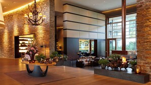 Eine geräumige Lobby mit Steinsäule, einem Kronleuchter, einer Sitzecke mit Sofas und einem Couchtisch sowie einem Kamin mit Pflanzen.