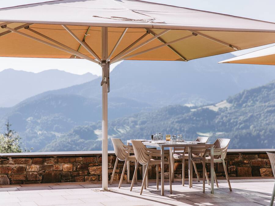 An outdoor dining area with a table and chairs under a large umbrella, overlooking a mountainous landscape.