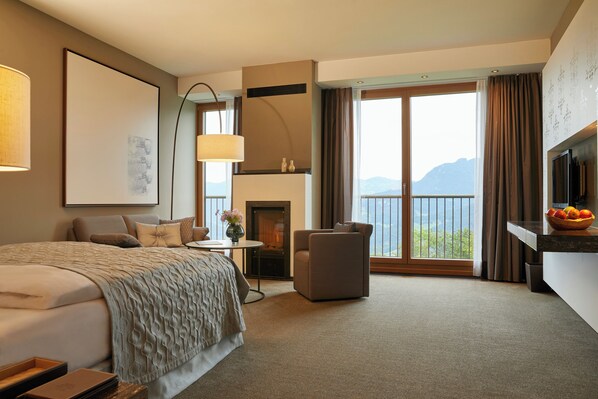 Un'ampia camera d'albergo con un letto grande, un'area salotto, un camino e un balcone con vista sulle montagne.