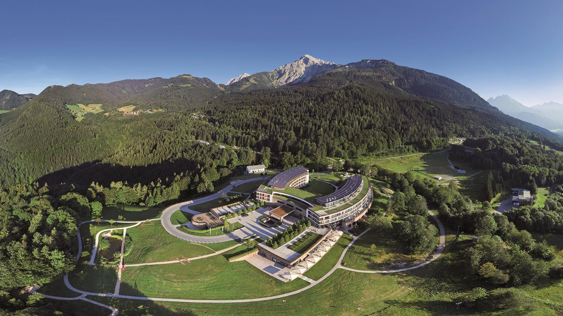 Vista aérea de un hotel moderno con un edificio curvo, rodeado de exuberante vegetación y montañas.