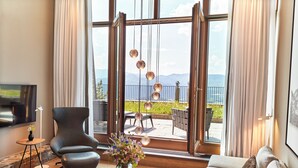 Ein modernes Wohnzimmer mit großem Fenster, einer Couch, einem Sessel, einem Fernseher und einer Vase mit Blumen.