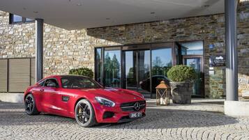 Une voiture de sport rouge est garée devant un hôtel aux murs en pierre et à l’entrée en verre.