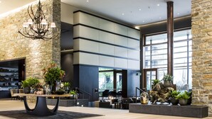 A modern lobby with a stone wall, a large chandelier, and a seating area with plants and a coffee table.