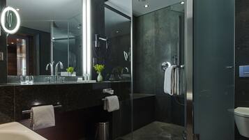 A modern bathroom with a glass-enclosed shower, a large mirror with a light, and a dark marble countertop.