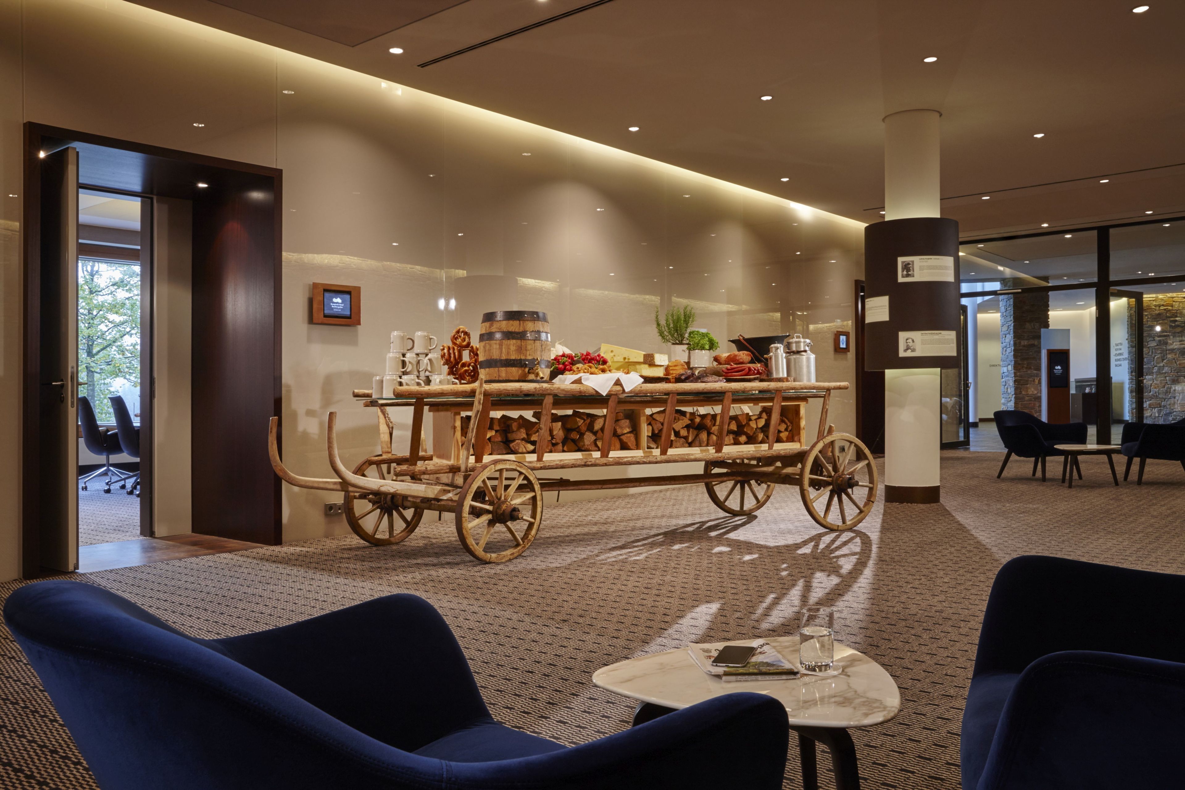 En modern entréhall med en central bardisk, en vagn i trä, sittplatser och ett litet bord med ett glas på.