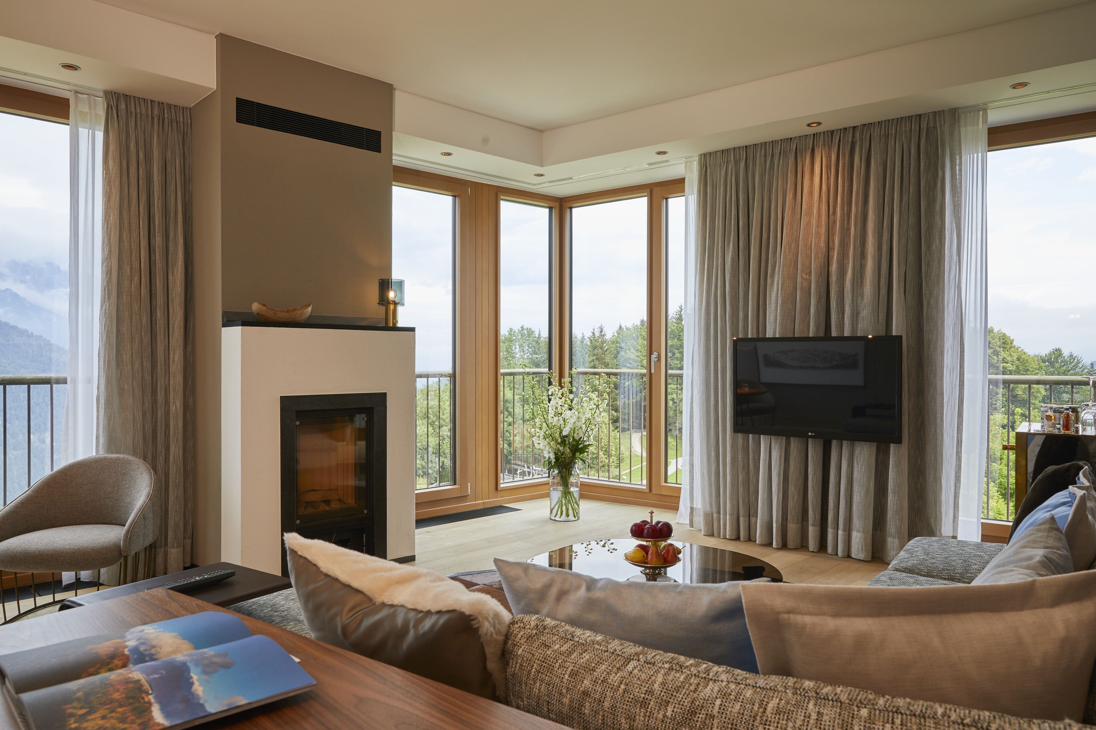 A modern living room with a fireplace, a flat-screen TV, and a large window offering a mountain view.