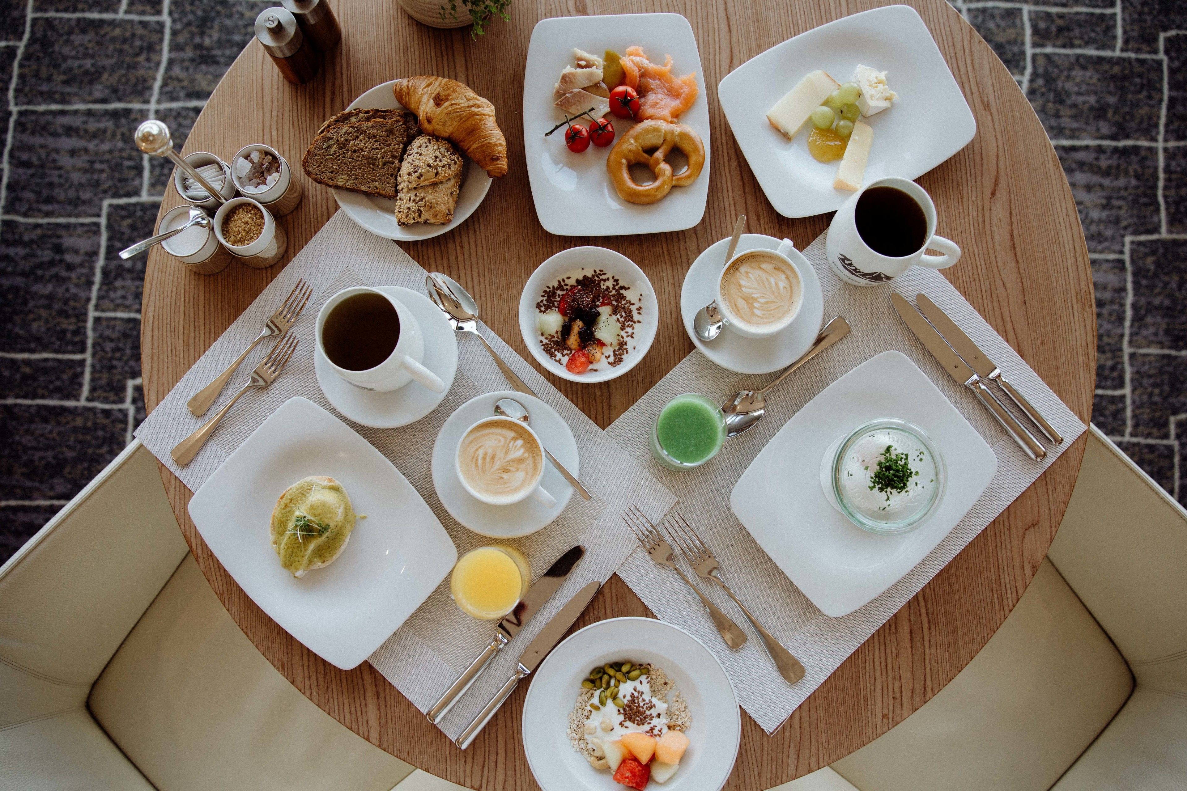 Una mesa redonda para comer con diversos alimentos de desayuno, como cruasanes, queso, frutas y bebidas.