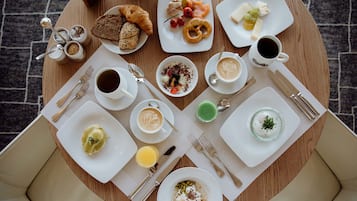 Una mesa redonda para comer con diversos alimentos de desayuno, como cruasanes, queso, frutas y bebidas.