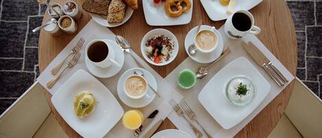 Una mesa redonda para comer con diversos alimentos de desayuno, como cruasanes, queso, frutas y bebidas.